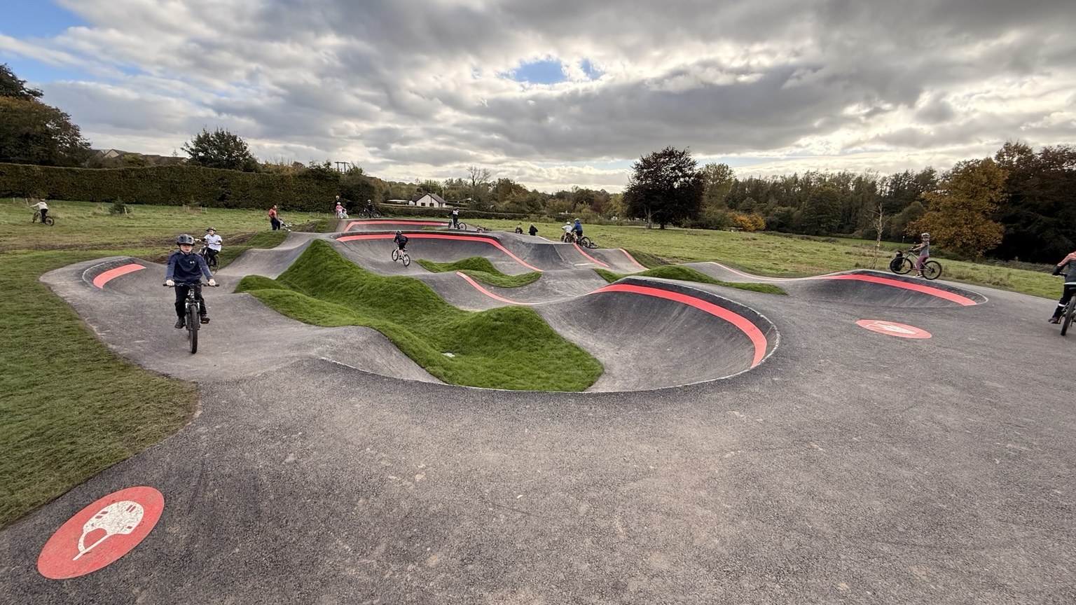 Riders using an asphalt pump track with rollers, banked turns and grassy islands